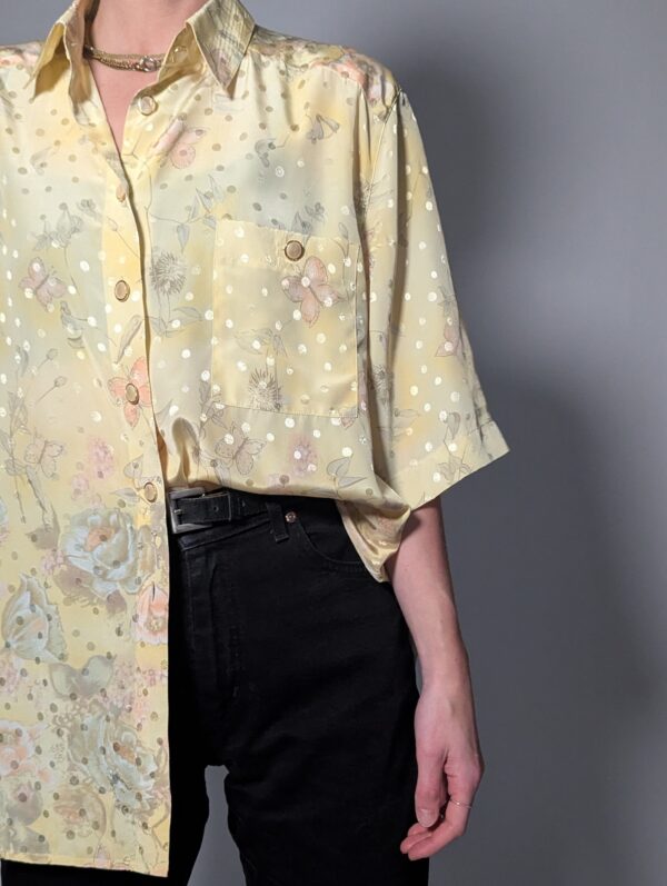 Pastelgele vintage blouse met korte mouwen, oversized fit, bloemenprint en subtiele stipdetails.