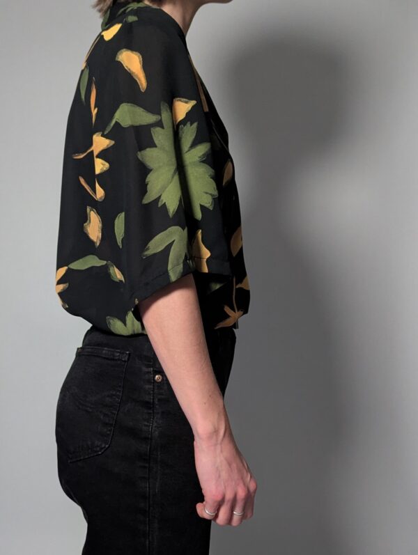 Zwarte vintage blouse met korte mouwen en grote bloemenprint in groen- en geeltinten.