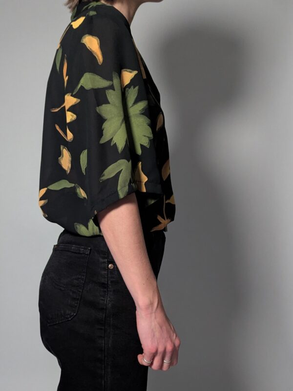 Zwarte vintage blouse met korte mouwen en grote bloemenprint in groen- en geeltinten.
