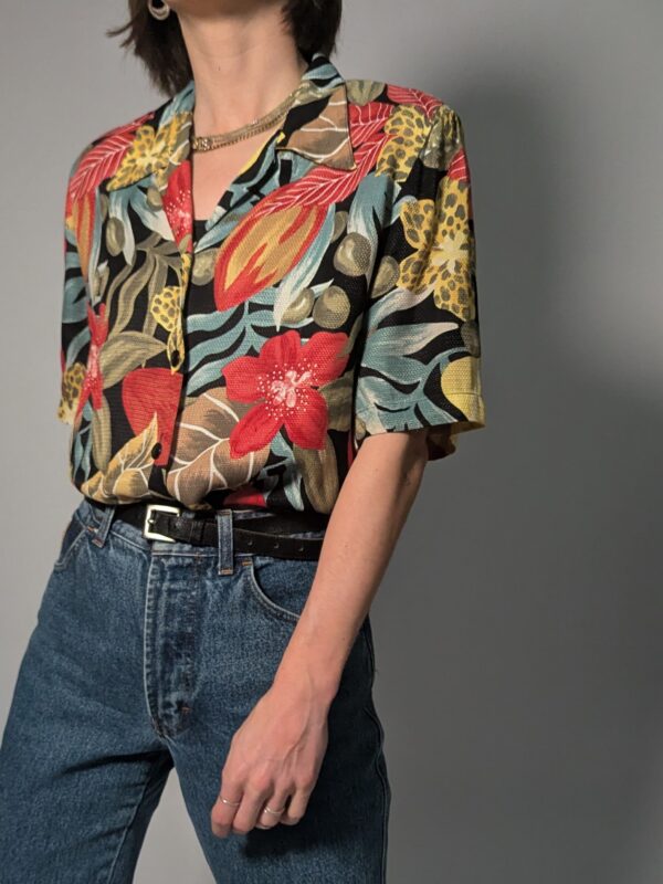 Vintage blouse met korte mouwen, zwarte basis en kleurrijke bloemen- en bladprint in rood, geel, groen en blauw.