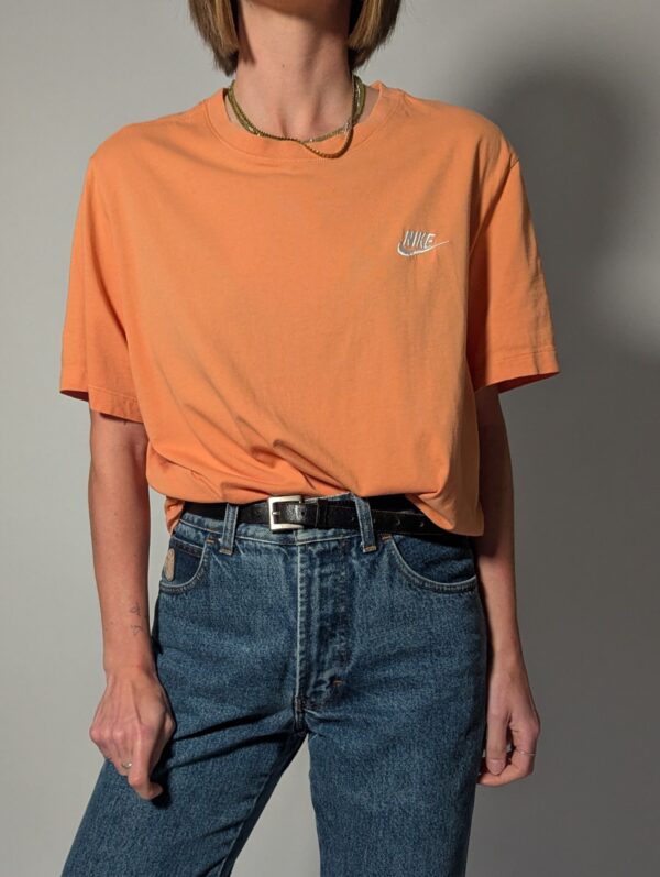 Vintage Nike T-shirt in zachte perziktint met korte mouwen, relaxte pasvorm en subtiel wit logo op de borst.