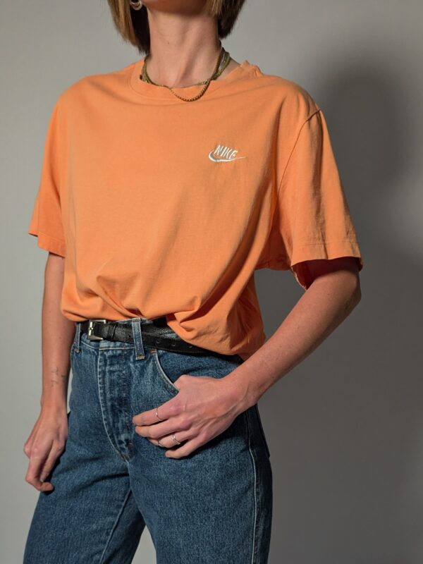 Vintage Nike T-shirt in zachte perziktint met korte mouwen, relaxte pasvorm en subtiel wit logo op de borst.