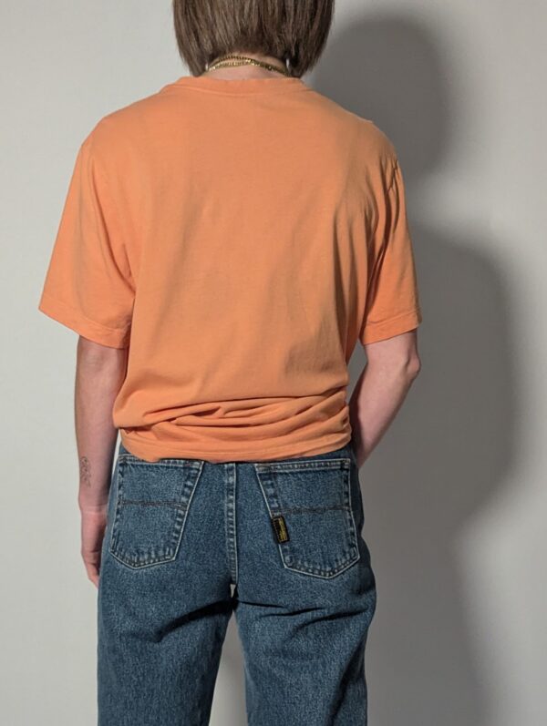 Vintage Nike T-shirt in zachte perziktint met korte mouwen, relaxte pasvorm en subtiel wit logo op de borst.