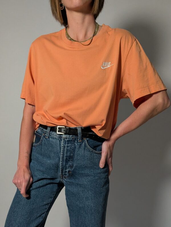 Vintage Nike T-shirt in zachte perziktint met korte mouwen, relaxte pasvorm en subtiel wit logo op de borst.