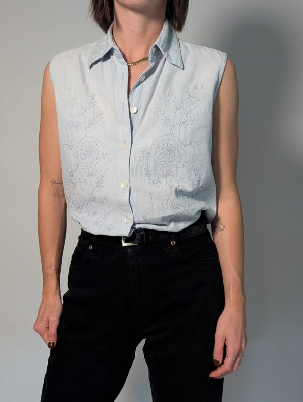 Vintage lichtblauwe mouwloze blouse met geborduurde bloemen, kraag en knoopsluiting.