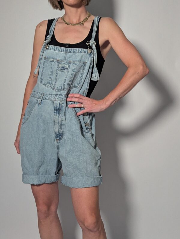 Denim overall 02 Vintage lichtblauwe denim overall met korte broekspijpen, verstelbare schouderbanden en relaxte pasvorm.