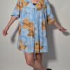 Vintage lichtblauwe blousejurk met grote bloemenprint in zand-, oker- en rozetinten, korte mouwen en knoopsluiting.