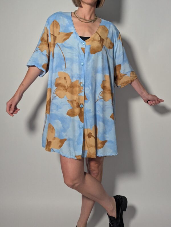 Vintage lichtblauwe blousejurk met grote bloemenprint in zand-, oker- en rozetinten, korte mouwen en knoopsluiting.