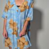 Vintage lichtblauwe blousejurk met grote bloemenprint in zand-, oker- en rozetinten, korte mouwen en knoopsluiting.