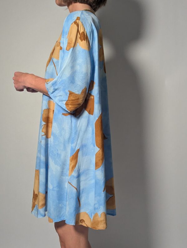 Vintage lichtblauwe blousejurk met grote bloemenprint in zand-, oker- en rozetinten, korte mouwen en knoopsluiting.