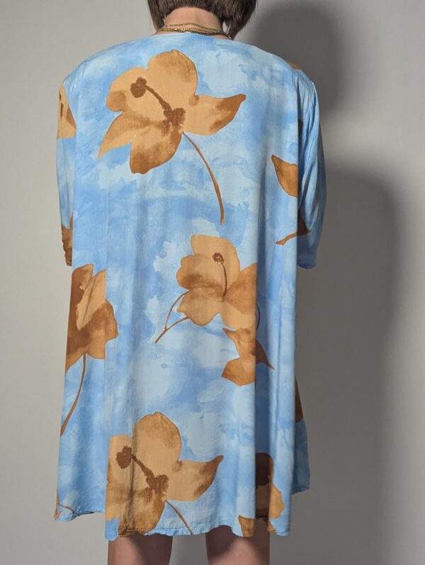 Vintage lichtblauwe blousejurk met grote bloemenprint in zand-, oker- en rozetinten, korte mouwen en knoopsluiting.