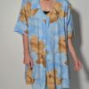 Vintage lichtblauwe blousejurk met grote bloemenprint in zand-, oker- en rozetinten, korte mouwen en knoopsluiting.