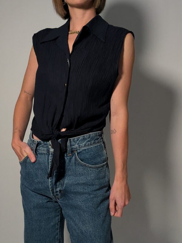 Nightfall tie 01 Vintage donkerblauwe mouwloze blouse met plisséstructuur, klassieke kraag, knoopsluiting en strikdetail aan de onderzijde.