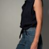 Vintage donkerblauwe mouwloze blouse met plisséstructuur, klassieke kraag, knoopsluiting en strikdetail aan de onderzijde.