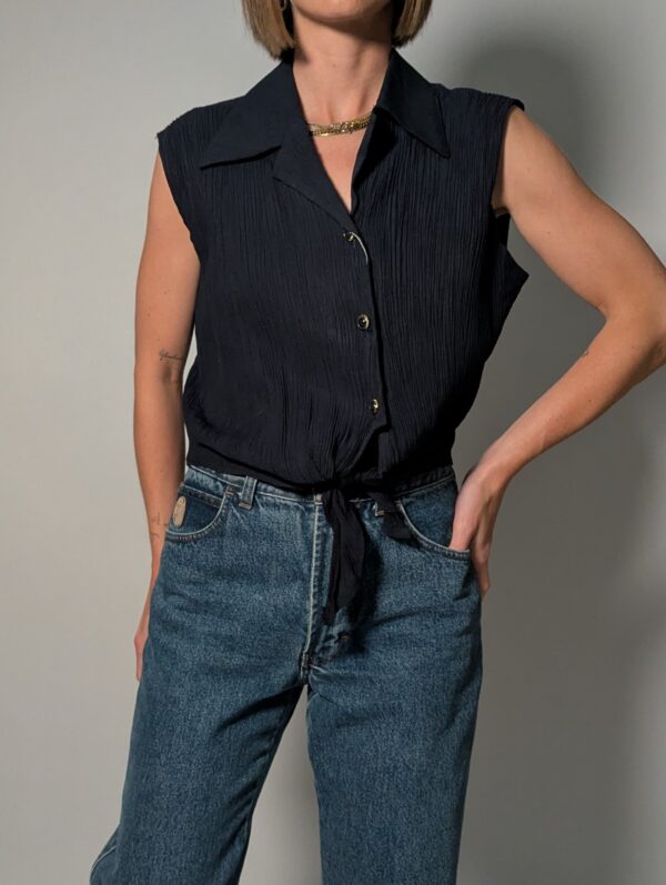 Vintage donkerblauwe mouwloze blouse met plisséstructuur, klassieke kraag, knoopsluiting en strikdetail aan de onderzijde.