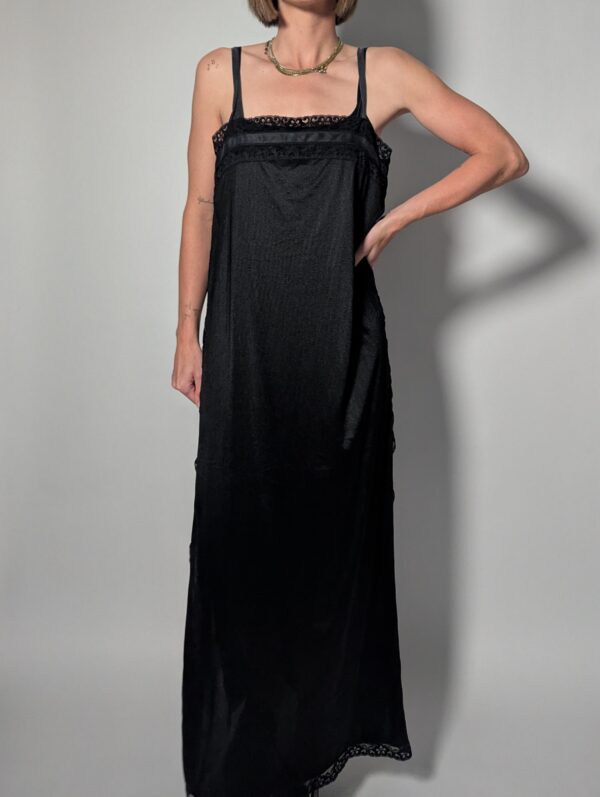 Vintage zwarte maxi jurk met smalle schouderbandjes, kanten details langs de hals en zoom en soepel vallende pasvorm.