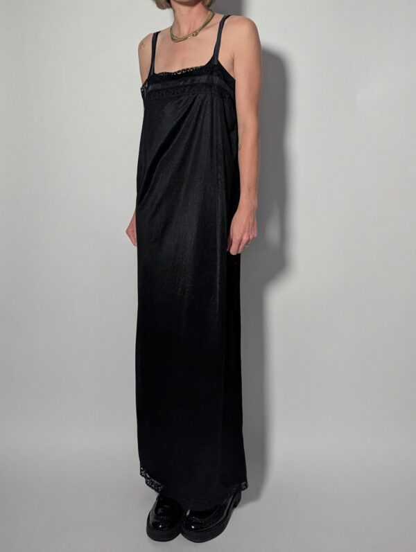 Vintage zwarte maxi jurk met smalle schouderbandjes, kanten details langs de hals en zoom en soepel vallende pasvorm.