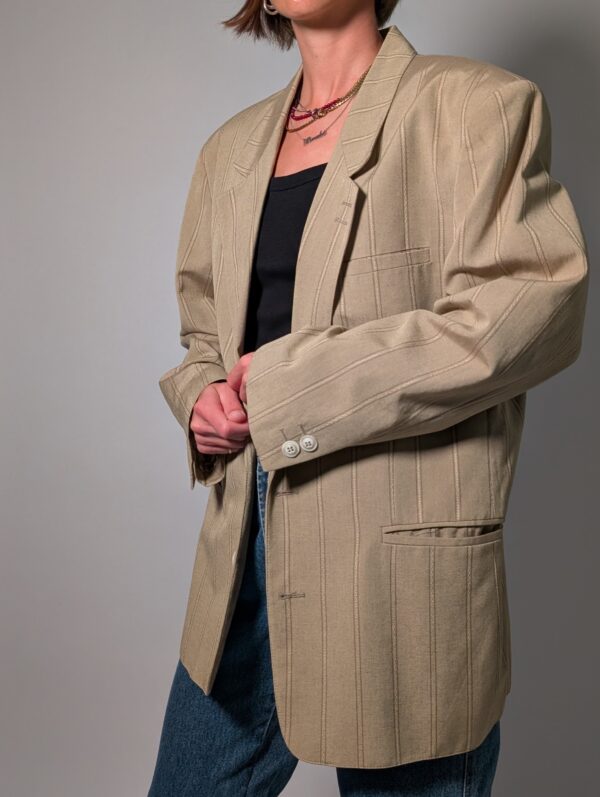 Sand stripe 01 Vintage beige blazer met subtiele verticale glansstrepen, klassieke revers en rechte licht oversized pasvorm.